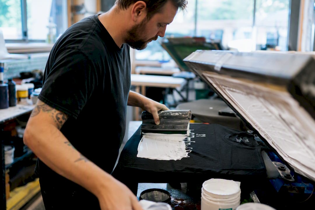 Ein Techniker bringt weiße Plastisolfarbe auf ein schwarzes T-Shirt auf.