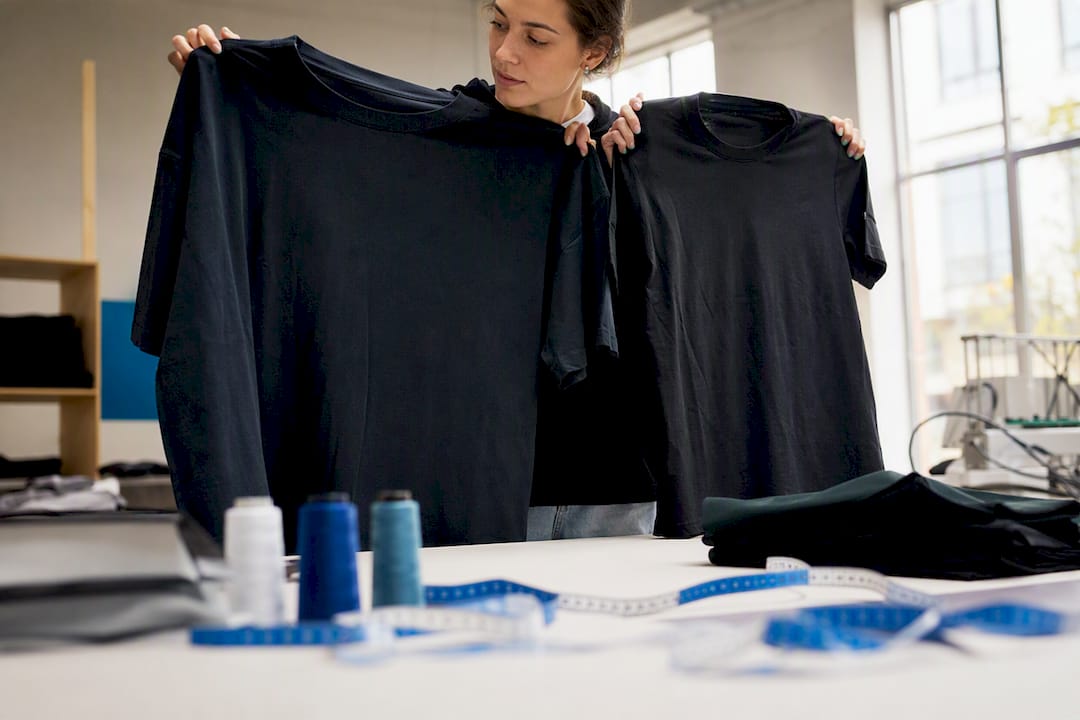 Hände vergleichen Stoffstücke in Oversize- und Regular-Fit-Passform